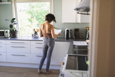 Woman looking at paper standing in kitchen - DMMF00064