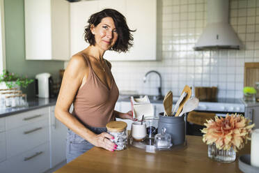 Lächelnde reife Frau vor der Kücheninsel zu Hause - DMMF00073