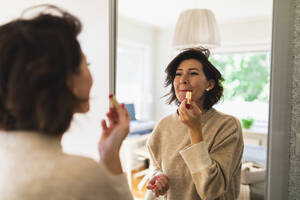 Mature woman looking in mirror and applying lipstick - DMMF00077