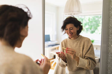 Glückliche Frau hält Lippenstift vor einem Spiegel zu Hause - DMMF00078