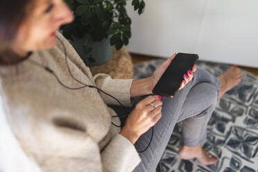 Frau mit Mobiltelefon, die zu Hause Musik über In-Ear-Kopfhörer hört - DMMF00107