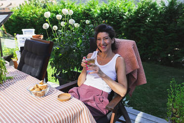 Happy woman holding cup at dining table on terrace - DMMF00113