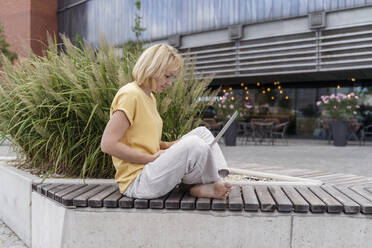 Mature blond freelancer using laptop on bench - TOF00114