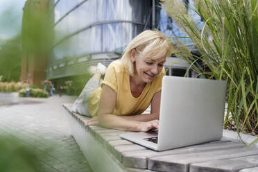 Glückliche Geschäftsfrau mit Laptop auf einer Bank liegend - TOF00120