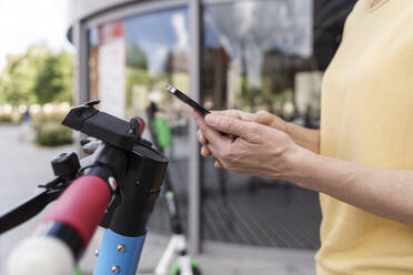 Die Hände einer Frau, die einen Elektroroller über ihr Smartphone mietet - TOF00122