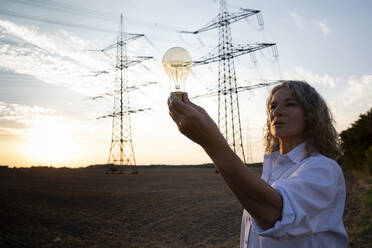 Ältere Frau betrachtet eine Glühbirne vor einem Strommast - FLLF00736