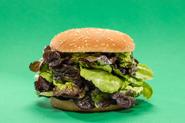 Fresh burger bun with bunch of fresh mesclun leaves as concept of healthy food against green background - ADSF38633