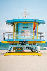 Blauer und gelber Rettungsschwimmerturm am Sandstrand gegen türkisfarbenes Meer und bewölkten Himmel an einem Sommertag in Miami, USA - ADSF38644