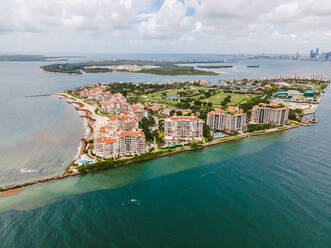 Luftaufnahme von mehrstöckigen Wohngebäuden in der Nähe von Sandstrand auf einer Insel unter bewölktem Himmel in Florida - ADSF38645