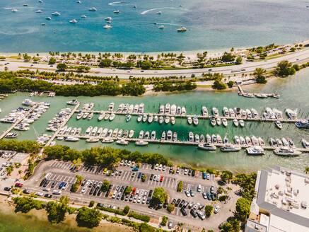 Drone view of modern boats moored in port amidst parking area and sandy beach of rippling ocean on sunny day in Miami Beach - ADSF38651