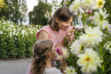 Mutter und Tochter riechen an Blumen im Garten - DIGF18832