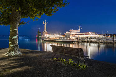 Deutschland, Baden-Württemberg, Konstanz, Hafen am Bodenseeufer bei Nacht mit leerer Bank im Vordergrund - DIGF18840