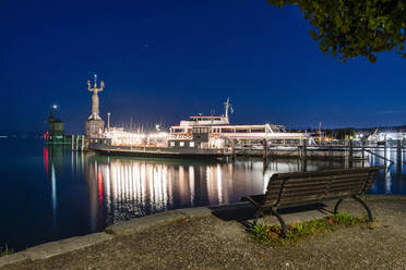 Deutschland, Baden-Württemberg, Konstanz, Hafen am Bodenseeufer bei Nacht mit leerer Bank im Vordergrund - DIGF18841