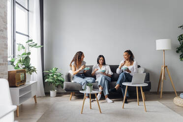 Young roommates with salad bowls sitting on sofa in living room - MEUF08040