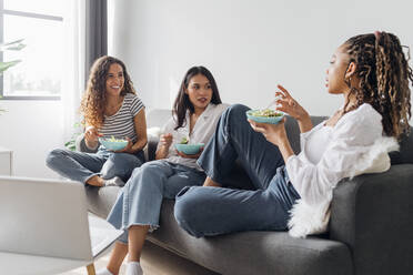 Junge Freunde unterhalten sich und essen zusammen Salat im Wohnzimmer zu Hause - MEUF08044