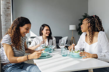 Cheerful friends having salad at dining table in living room - MEUF08045