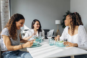Fröhliche Freunde essen Salat am Esstisch im Wohnzimmer - MEUF08045