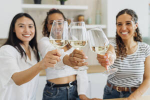 Fröhliche junge Mitbewohner stoßen in der Küche zu Hause mit Weingläsern an - MEUF08056