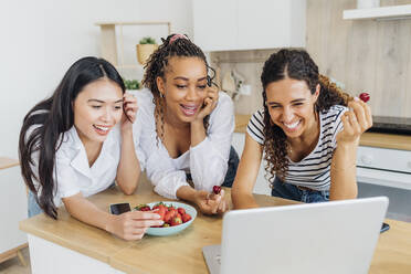 Glückliche Freunde essen Obst und führen einen Videoanruf auf dem Laptop zu Hause - MEUF08064