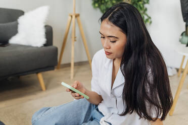 Woman with long hair using smart phone sitting at home - MEUF08071