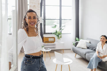 Smiling young woman opening door in living room at home - MEUF08079