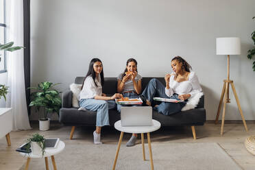 Young friends watching movie and eating pizza on sofa in living room - MEUF08084