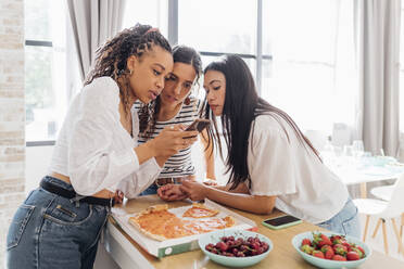 Frau teilt Smartphone mit Freunden in der Küche zu Hause - MEUF08089