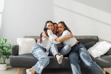 Glückliche Freunde, die sich gegenseitig umarmen, sitzen auf der Couch im Wohnzimmer - MEUF08104
