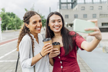 Smiling woman taking selfie with friend on smart phone - MEUF08110