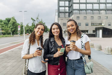 Lächelnde multirassische Freunde mit wiederverwendbaren Kaffeebechern auf dem Fußweg stehend - MEUF08112