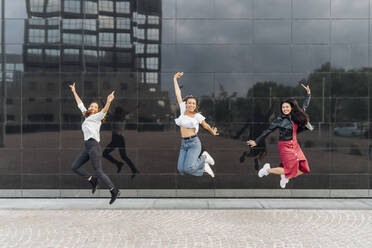 Fröhliche Freunde springen vor einer Glaswand - MEUF08122