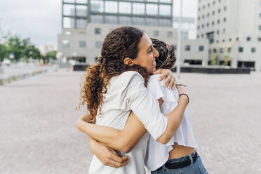 Happy women embracing each other on footpath - MEUF08123