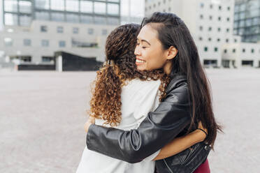 Smiling woman hugging friend on footpath - MEUF08124