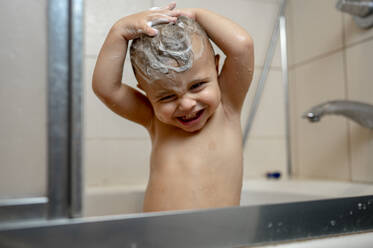 Happy baby boy washing hair in bathtub - ANAF00049