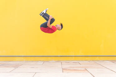 Männlich springt in der Nähe von gelben Wand und zeigt Purzelbaum beim Parkour in der Stadt an einem sonnigen Tag - ADSF38700