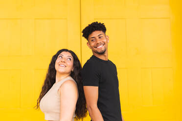 Porträt eines selbstbewussten jungen Paares, das Rücken an Rücken vor einer gelben Tür steht - ADSF38740