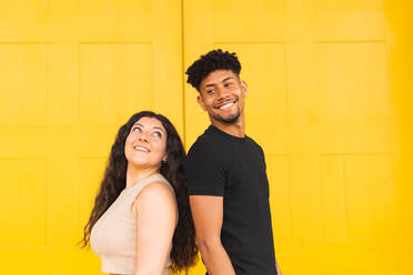 Portrait of confident young couple standing back to back against yellow door - ADSF38740