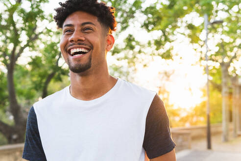 Cheerful young man looking away while standing at park - ADSF38743