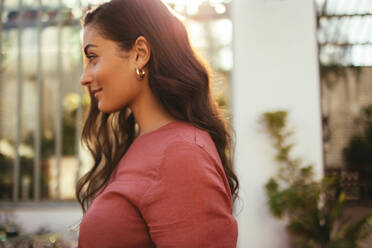 Attractive young tourist woman standing outdoors during the day. Elegant young woman looking cheerful outside a luxury hotel. Young woman vacationing alone at a holiday resort. - JLPPF00267