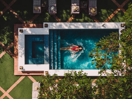 Draufsicht auf eine junge Touristin, die sich beim Schwimmen allein auf dem Wasser treiben lässt. Attraktive junge Frau, die sich in einem Pool eines Luxushotels entspannt. Junge Frau, die allein in einem Ferienort Urlaub macht. - JLPPF00277