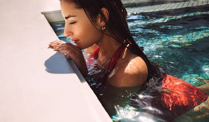 Beautiful young woman swimming alone while on a summer vacation. Young tourist woman leaning on the edge of a swimming pool with her eyes closed. Woman unwinding at a luxury holiday resort. - JLPPF00282