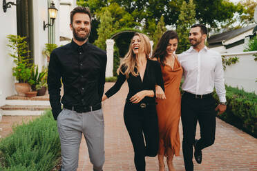 Friends walking outside a hotel in formal wear. Two happy couples smiling cheerfully while walking together at a luxury hotel. Group of friends arriving at a social event during vacation. - JLPPF00314