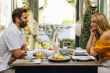 Ehepaar mittleren Alters, das einen romantischen Urlaub zusammen genießt. Glückliches Ehepaar beim Frühstück in einem Urlaubsort. Das Paar sieht sich liebevoll an, während es zusammen am Esstisch sitzt. - JLPPF00349