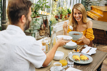 Glückliches Ehepaar, das fröhlich lächelt, während es gemeinsam an einem Esstisch isst. Ein Paar mittleren Alters, das einen romantischen Urlaub in einem Ferienort genießt. - JLPPF00350