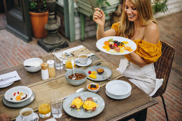 Fröhliche Touristin, die ein gesundes Frühstück in einem Luxushotel genießt. Glückliche Frau, die lächelt, während sie einen Teller mit Essen hält. Frau, die ihren Sommerurlaub in einem Ferienort genießt. - JLPPF00356
