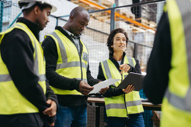 Mature woman having a discussion with her colleagues in a distribution warehouse. Group of multicultural employees having a staff meeting in a logistics centre. - JLPPF00393