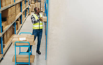 Warehouse picker pulling a flat box from a shelf while wearing a headset. Logistics worker fulfilling multiple orders with voice instructions from a warehouse management system. - JLPPF00412