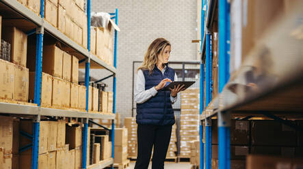 Female logistics worker doing stock control using warehouse management software in a warehouse. Woman checking shipping labels against an inventory list on a digital tablet. - JLPPF00426