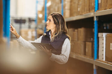 Female logistics employee checking shipping labels against an inventory list on a digital tablet. Woman doing inventory control using warehouse management software. - JLPPF00428