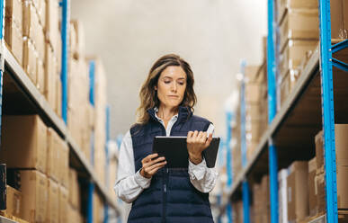Eine weibliche Lagerarbeiterin sieht sich eine Inventarliste auf einem digitalen Tablet an. Eine Frau arbeitet mit einem digitalen Lagerverwaltungssystem in einem modernen Vertriebszentrum. - JLPPF00437